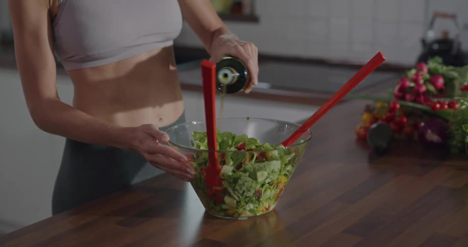 A woman in the kitchen putting oil in a salad in a bowl