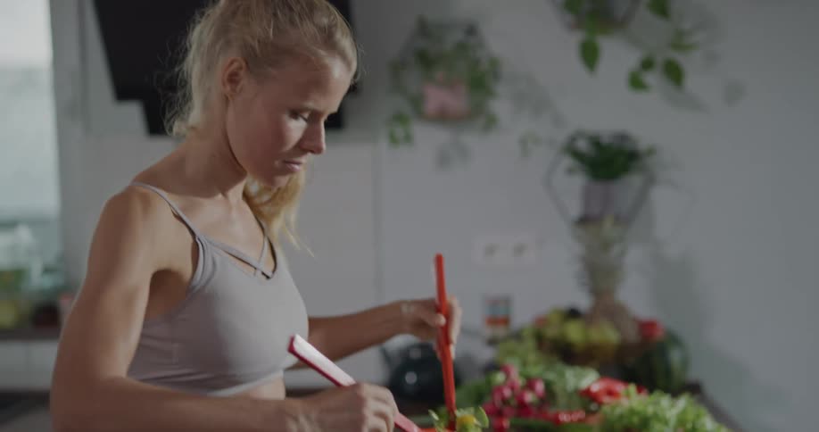 A young woman mixes a salad together in her kitchen