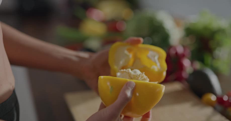 A woman cutting a yellow bell pepper in half and pulling out the seeds