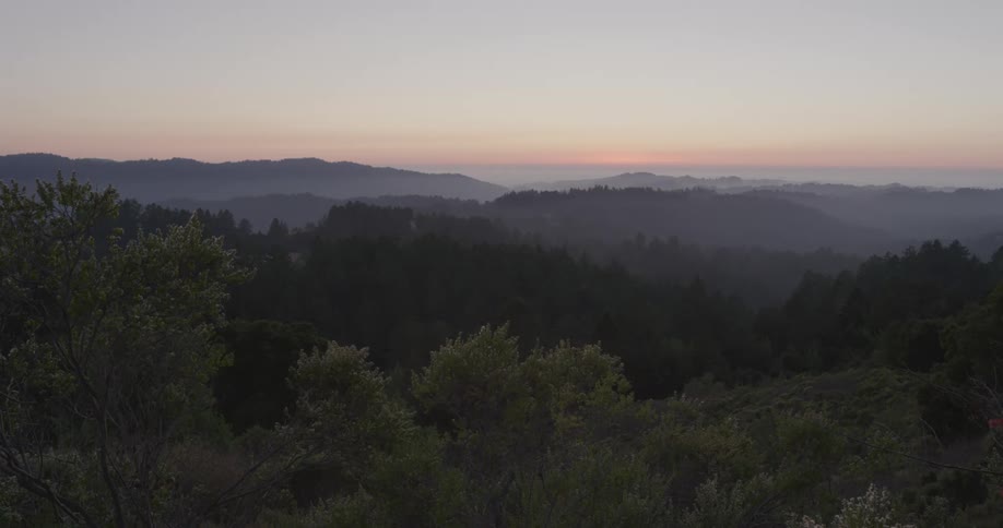 Fog covers forest and mountains all the way to red sky on the horizon