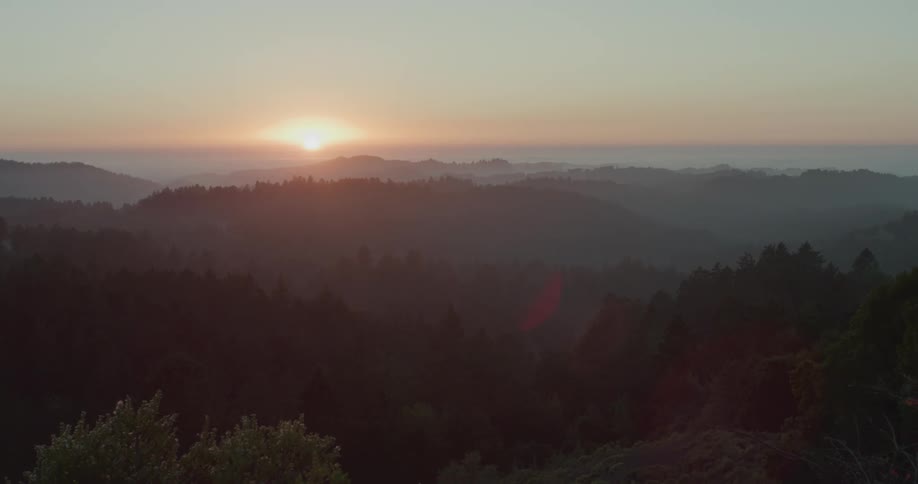Sun rises on horizon turning sky red as fog obscures mountains and forest