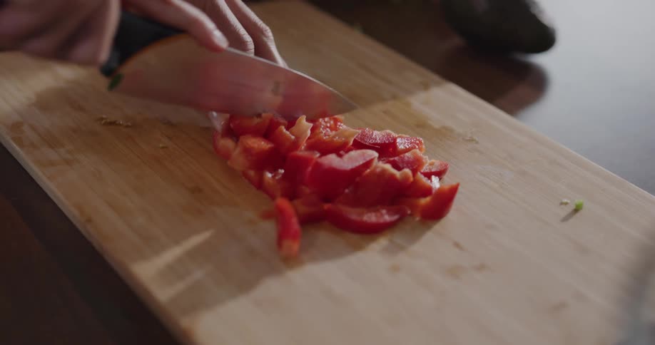 Woman cuts a red bell pepper on a cutting board in the kitchen