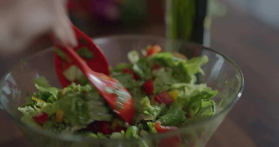 A woman pours oil on a salad and mixes it