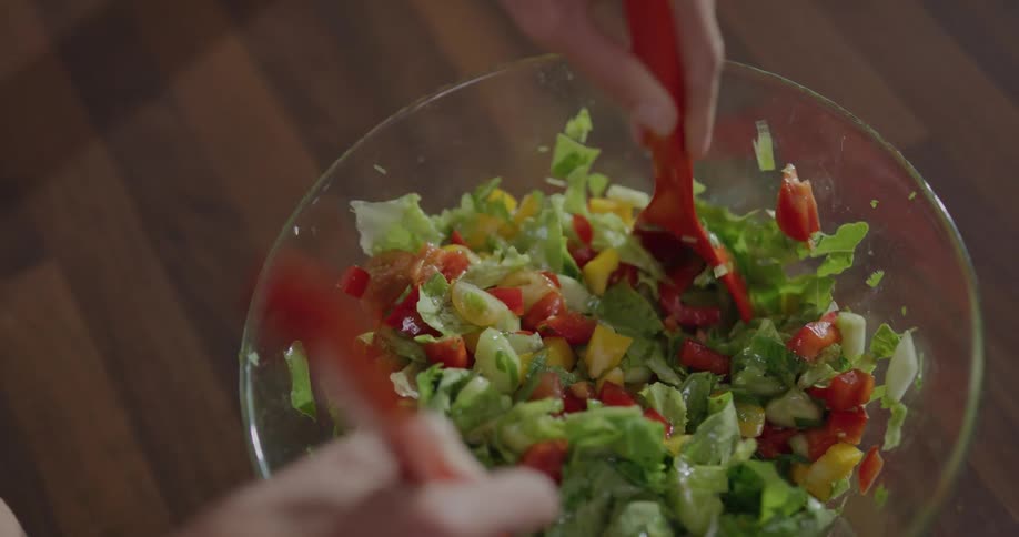 Woman stirs salad with two red spoons in the kitchen