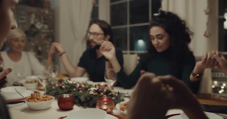 A family sitting at a dinner tables joins hands and prays before a meal