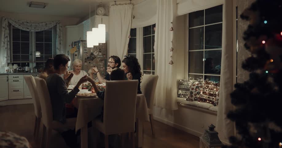 A group of people sitting around a dining table hold hands as grace is said