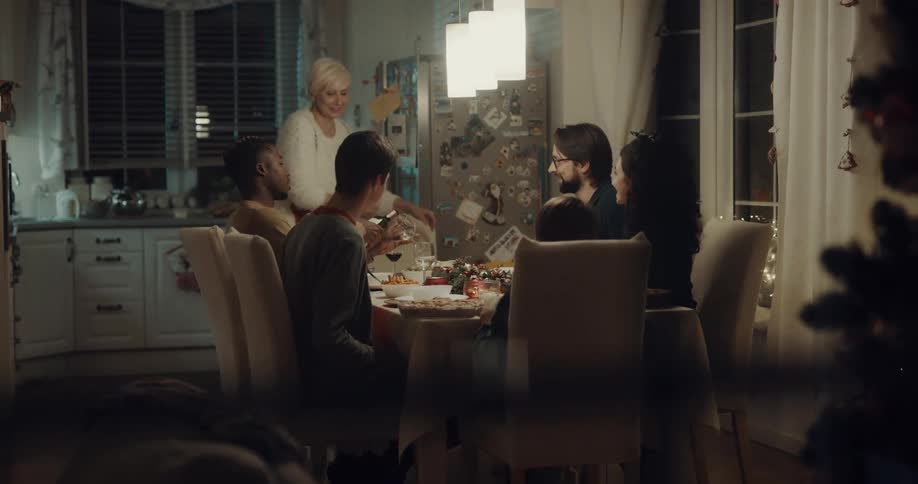 A group of young adults sit around a dining table with an older woman as their host