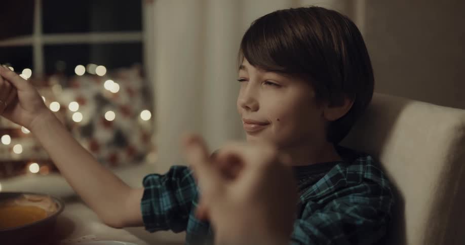 A boy peaks around him as he holds hands and bows his head in prayer with others around a dining table