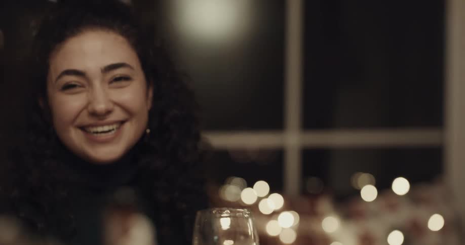 A young woman drinking wine at a dinner table laughs and her boyfriend leans over and kisses her