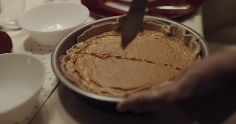 A woman standing at the dinner table cuts a pie