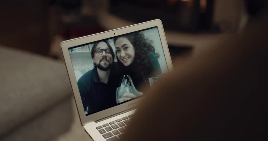 A couple uses a laptop to video chat with other couple while sitting on the sofa in the living room of a house