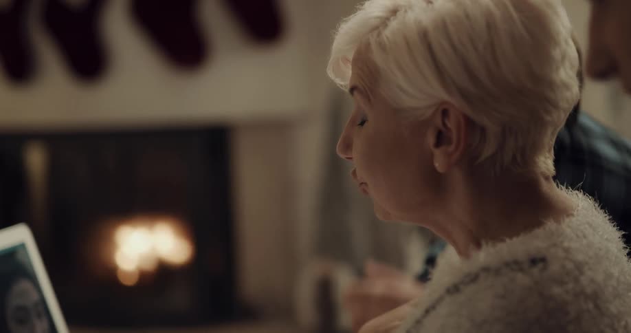 Woman and youths in room with christmas stockings near fireplace video call with woman
