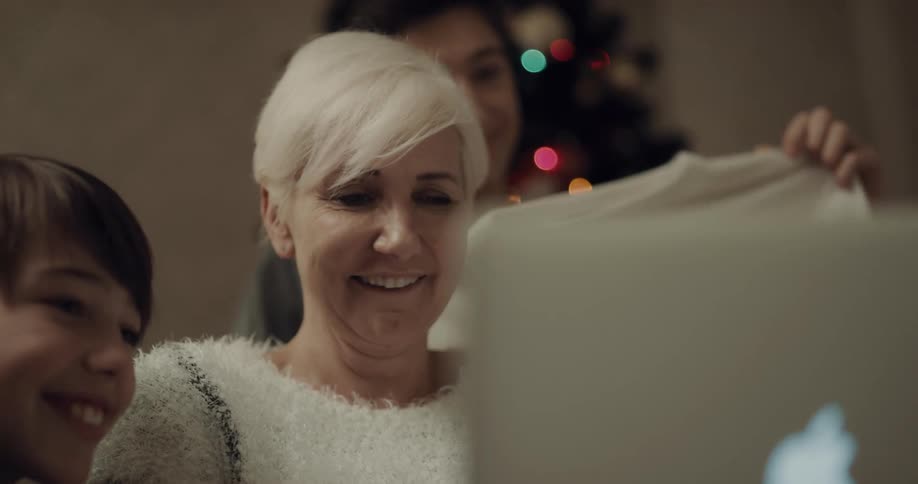 An elderly woman and her grandchildren laugh while looking at a laptop together