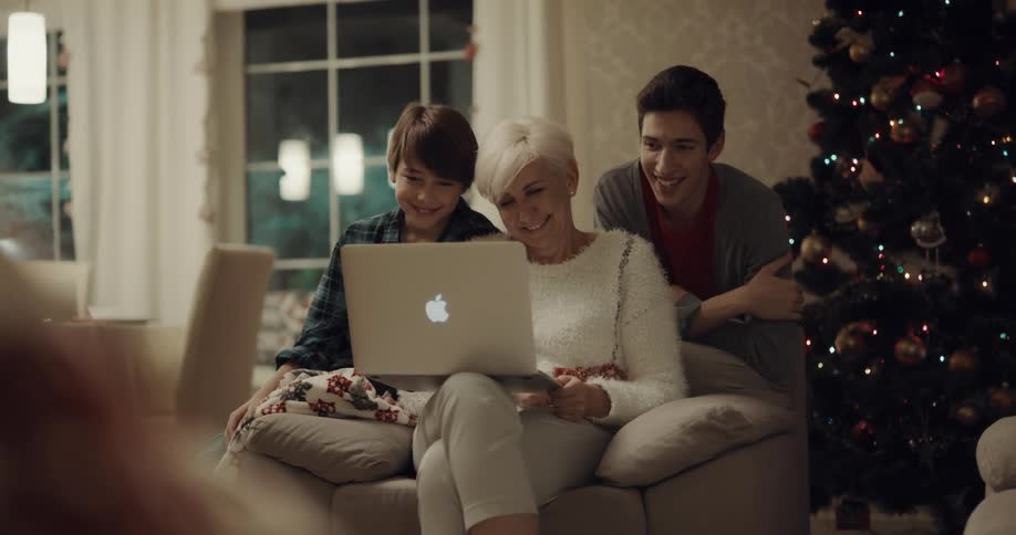 A woman holds a laptop and laughs as she looks at it with her two grandsons