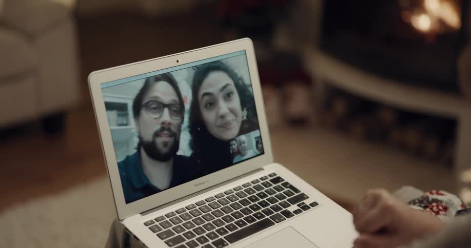 A person sits with a laptop in their lap having a video call with a man and woman