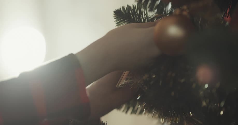 Person hangs ornaments on christmas tree while another walks past