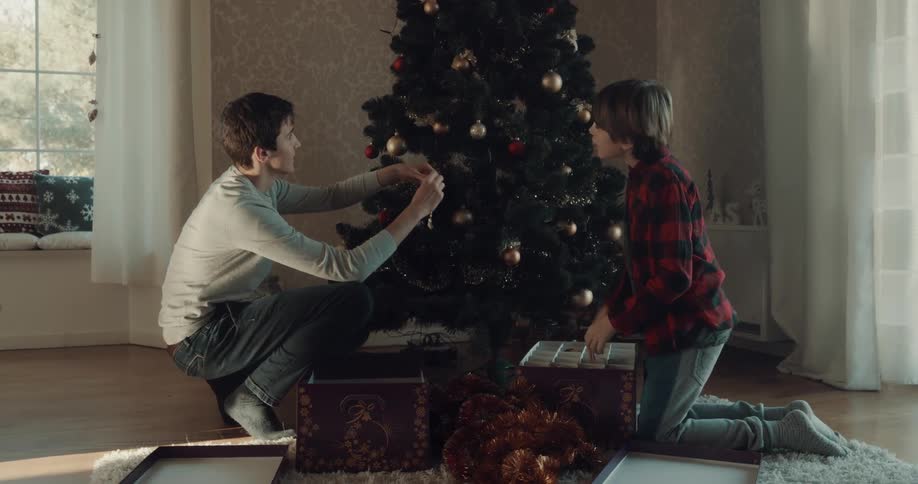 Brothers run into living room carrying boxes of ornaments and start decorating christmas tree