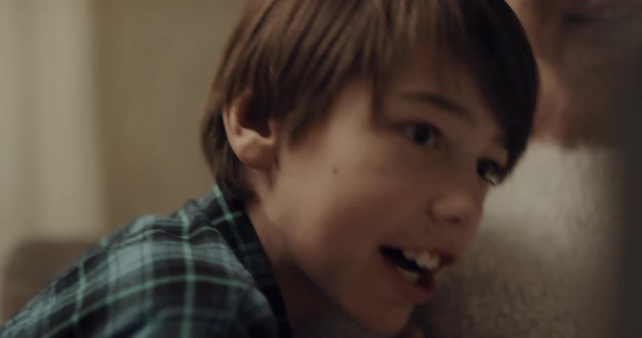 Two boys laugh and talk with their grandmother in front of a christmas tree