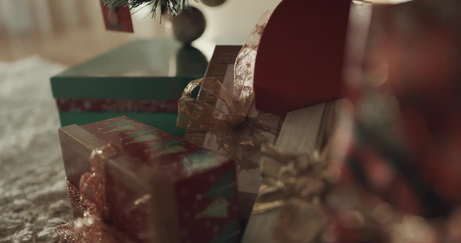 A pile of presents with ribbons on them lying on the floor beneath a christmas tree