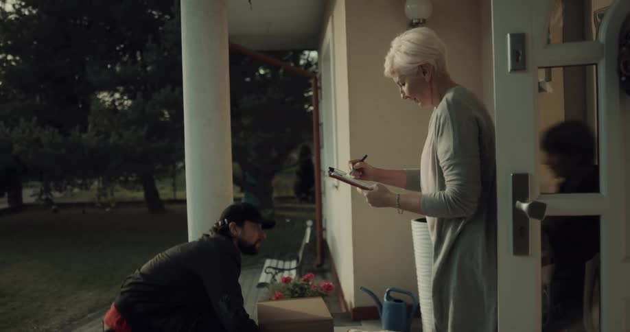 A delivery man delivers a stack of packages to the house of an elderly woman and her grandson who gives him a gift in return