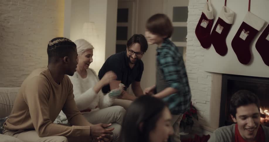 A young boy takes his grandmother a christmas present as other people chat and play a game