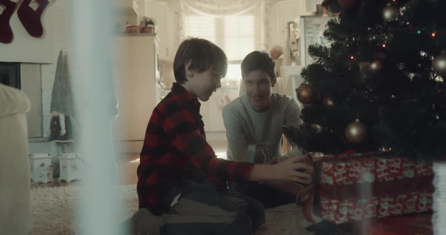 Two boys sit at a christmas tree and organize gifts under the tree