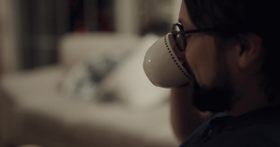 Man sits in living room talking and smiling while drinking from coffee cup