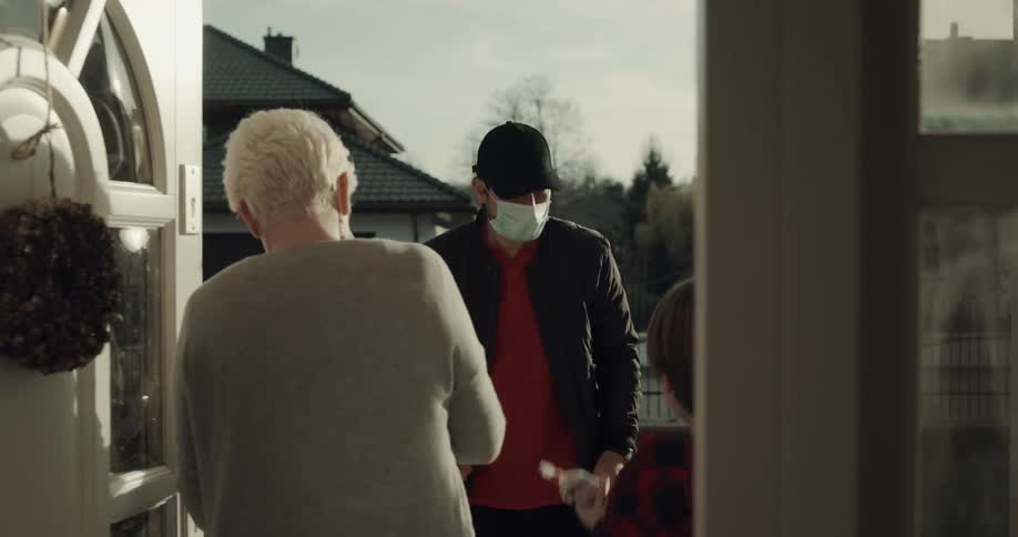 A man with a hat and a mask delivering boxes to a woman and boy