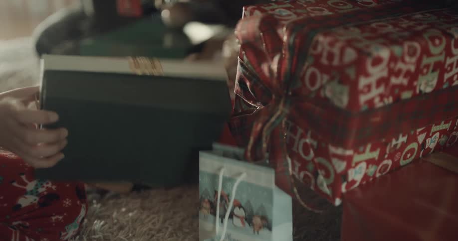 A pair of children in their pajamas retrieve gifts from below a christmas tree
