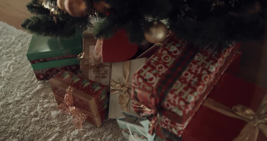 A pile of presents on the floor beneath a christmas tree