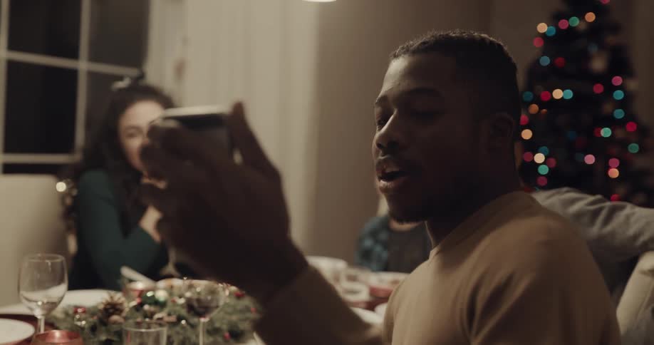 A group of people sit at the dinner table and wave at someone on a cell phone