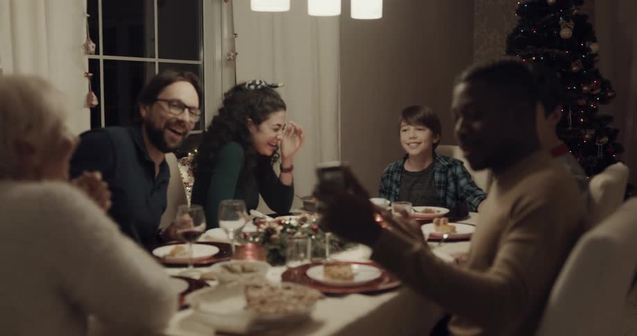 Man turns mobile phone to allow people at christmas dinner to wave and interact with woman on video call
