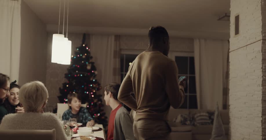 Friends and family laugh and talk over dinner during christmas then one gets up to make call