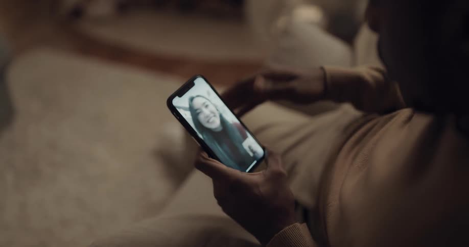 Man with a brown sweatshirt makes a video call on his smartphone with woman in the living room at home