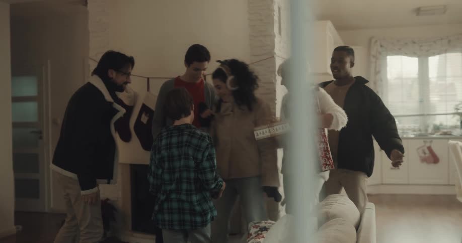 A group of men and women greet each other in front of a fireplace decorated with stockings