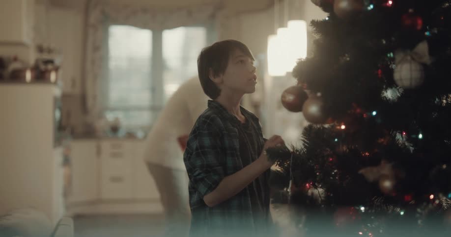 Son decorates the christmas tree and cuddles his father who brings presents