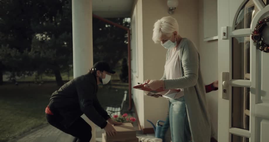 A man with a hat and a mask delivering boxes to a woman and boy