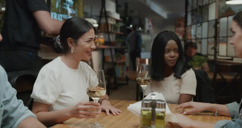 Server brings wine and beer to table friends are laughing and talking at