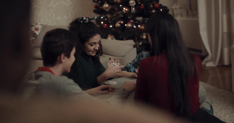 People sit on rug playing cards near christmas tree
