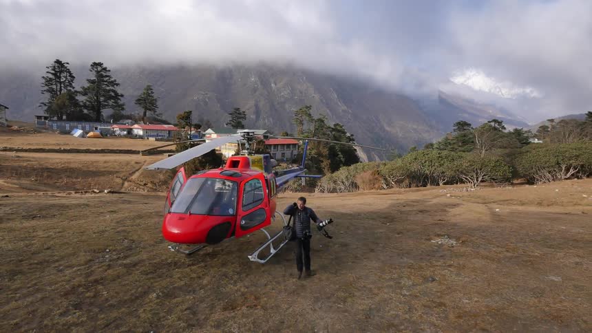 A man exiting a helicopter that has landed in the mountains near a residential area