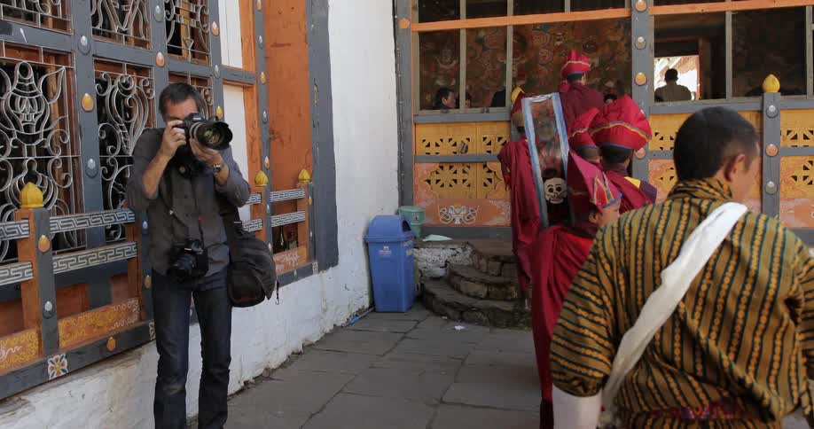 A photographer takes pictures of young buddhist monks carrying instruments into a building
