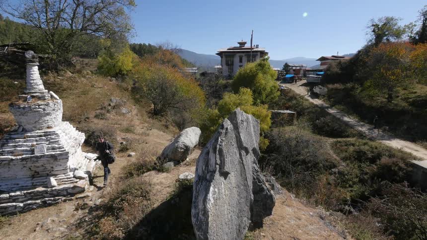 A man carrying a camera walks down a trail near a buddhist temple