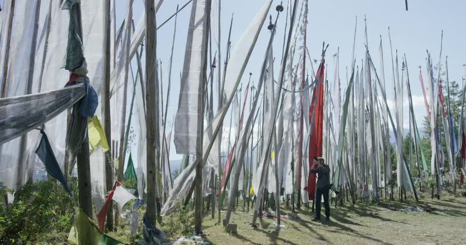 A row of poles with flags on them are being photographed by a man