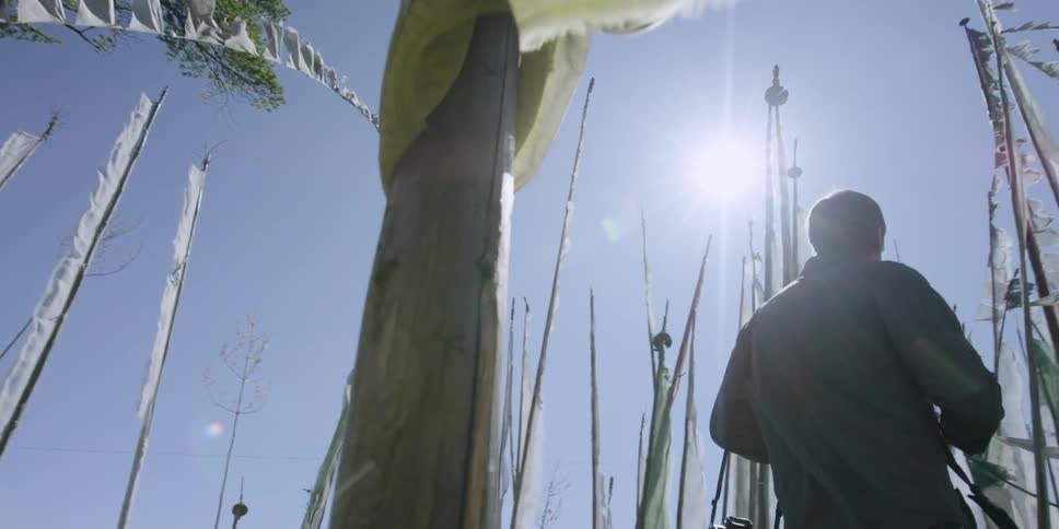 A man is walking between flag poles holding a camera