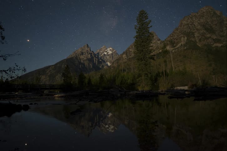 A placid lake at the base of a mountain reflects the sky as the sun rises