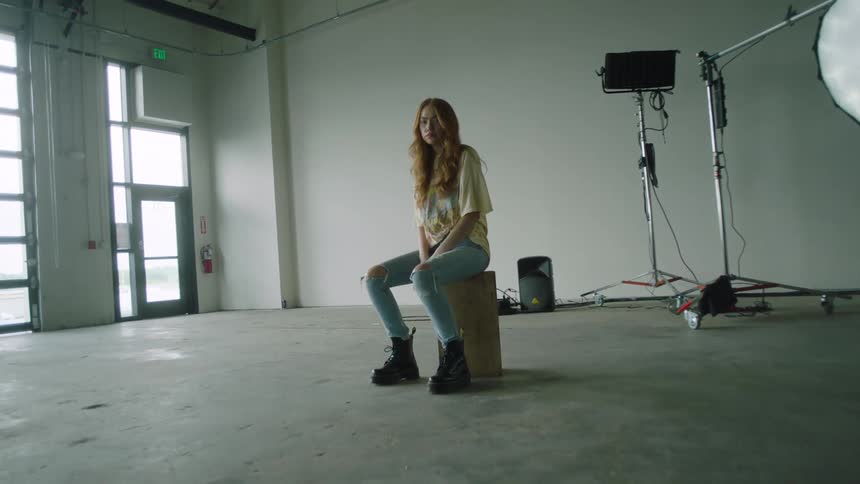 A woman in a room sitting on a box with a wall and a door in the background