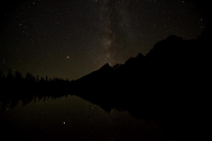 Stars in a nighttime sky above a mountain and lake