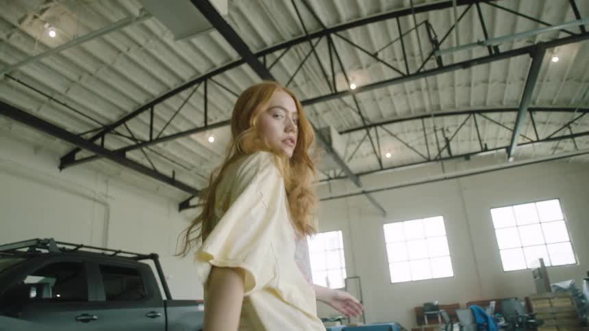 A young woman walks through a building while staring into the camera