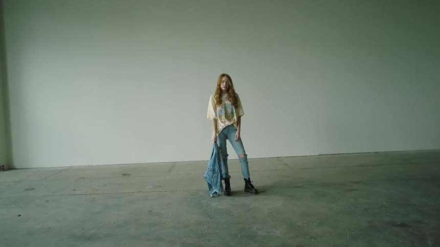 A teenage girl standing in an empty building holding a coat
