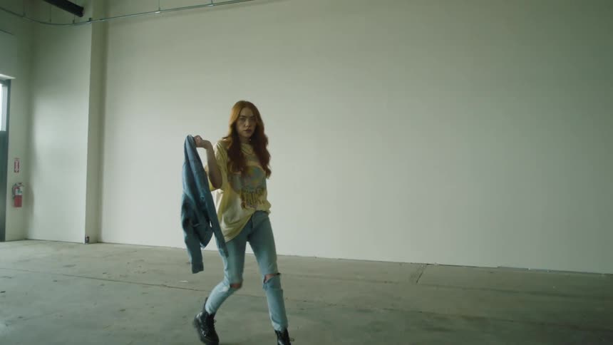 Woman carries her jacket over her shoulder as she walks in a large empty room while a man walks across from her